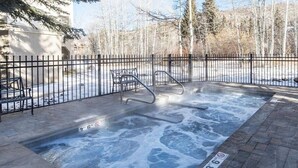 A hot tub area with a metal fence, a metal chair, and a paved walkway. - Charlie's Slopeside: Ski-In/Out Penthouse, Creekside, Sleeps 7, Hot Tub, Walk to Ski School (Beaver Creek)