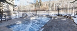 A hot tub area with a metal fence, a metal chair, and a paved walkway.