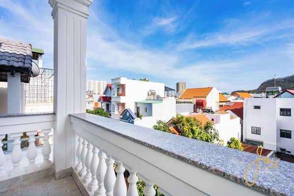 Ein Balkon mit weißer Brüstung, der auf ein Wohngebiet mit verschiedenen Gebäuden und blauem Himmel blickt.