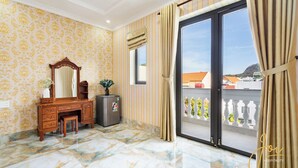 A hotel room with a marble floor, a wooden vanity with a mirror, a small refrigerator, and a view of the outside balcony.
