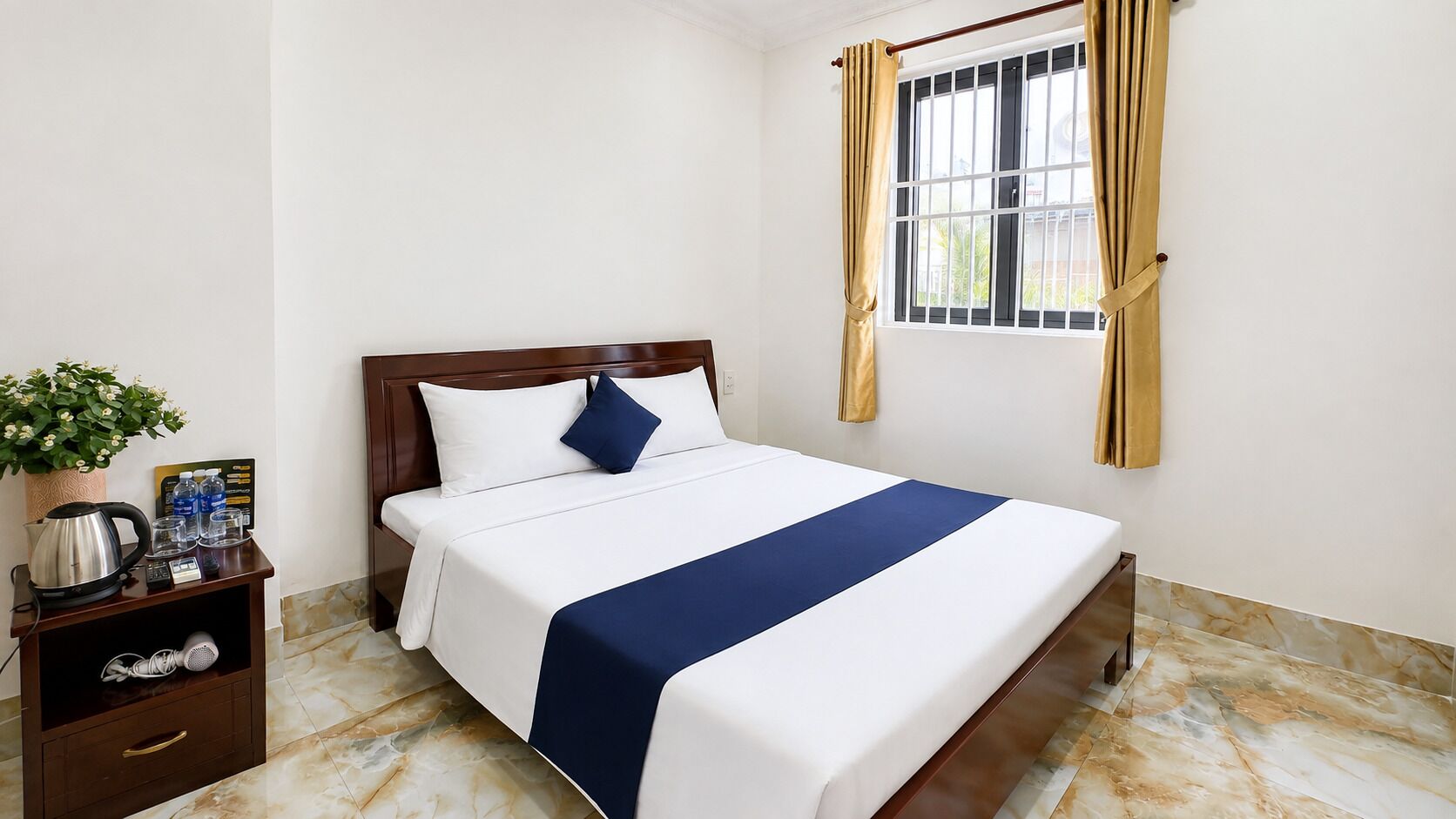 Una habitación de hotel con cama, mesita de noche con tetera, una planta y ventana con cortinas.