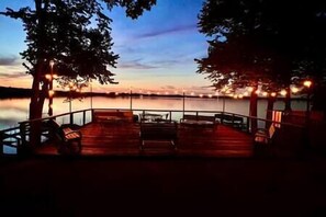 A wooden deck with outdoor seating and a view of a lake at dusk. - The Nest at Darling Shores (Alexandria)