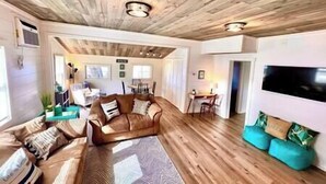 Ein geräumiges Wohnzimmer mit Holzbalkendecke, einem großen Sofa, einem Couchtisch und einem an der Wand befestigten Fernseher.