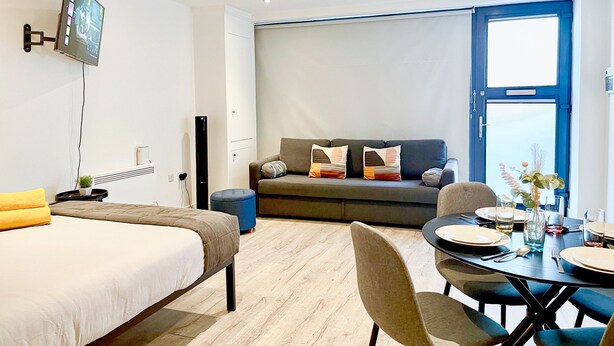 Ein modernes Hotelzimmer mit Bett, Sofa, Esstisch für zwei Personen und einem an der Wand befestigten Fernseher.