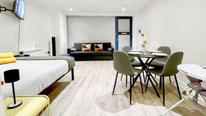 Ein modernes Hotelzimmer mit einem Bett, einem Essbereich mit Stühlen und Tisch, einer Couch und einem an der Wand befestigten Fernseher.