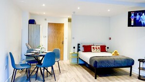 Ein modernes Schlafzimmer mit Bett, Nachttischen, Fernseher, Schreibtisch mit Stühlen und Holztür.