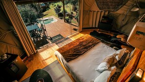 A tented accommodation with a bed, a desk, and a view of a pool and garden. - Esphera Glamping - Gravataí - RS (Gravatai)