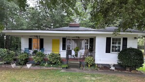 A single-story house with a porch, a yellow door, and a brick chimney. - Cozy private efficiency located near downtown Raleigh, PNC Arena, NCSU, RTP, RDU (Raleigh)