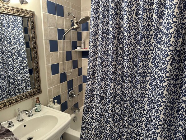 A bathroom with a sink, mirror, shower, and patterned curtain.