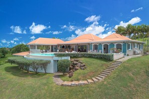 Una casa espaiosa amb piscina, un porxo cobert i una escala de pedra que condueix a l'entrada.