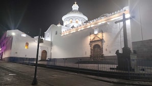 Un edificio blanco con una cúpula grande y una entrada más pequeña con una reja.