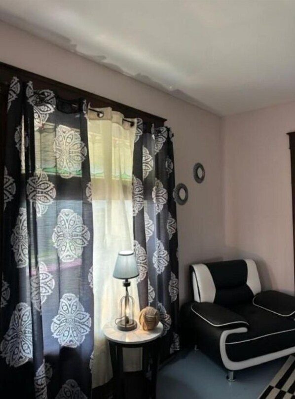 Een kamer met een gordijn in zwart-wit patroon, een klein rond tafeltje met een lamp, en een zwart-witte bank.