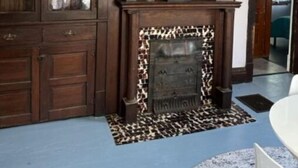 A room with a wooden cabinet, a fireplace with a patterned surround, and a framed cityscape picture on the wall. - Cozy home away from home.  Located in Steubenville. (Steubenville)