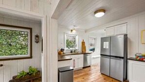 A modern kitchen with white cabinetry, stainless steel appliances, and wooden flooring. - Stone Cabin Retreat - Dog Friendly - Only 1.5mi to town & access to free trolley (Gatlinburg)