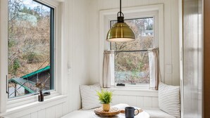 A cozy seating area with a window seat, a small table with a mug, and a hanging light fixture. - Stone Cabin Retreat - Dog Friendly - Only 1.5mi to town & access to free trolley (Gatlinburg)