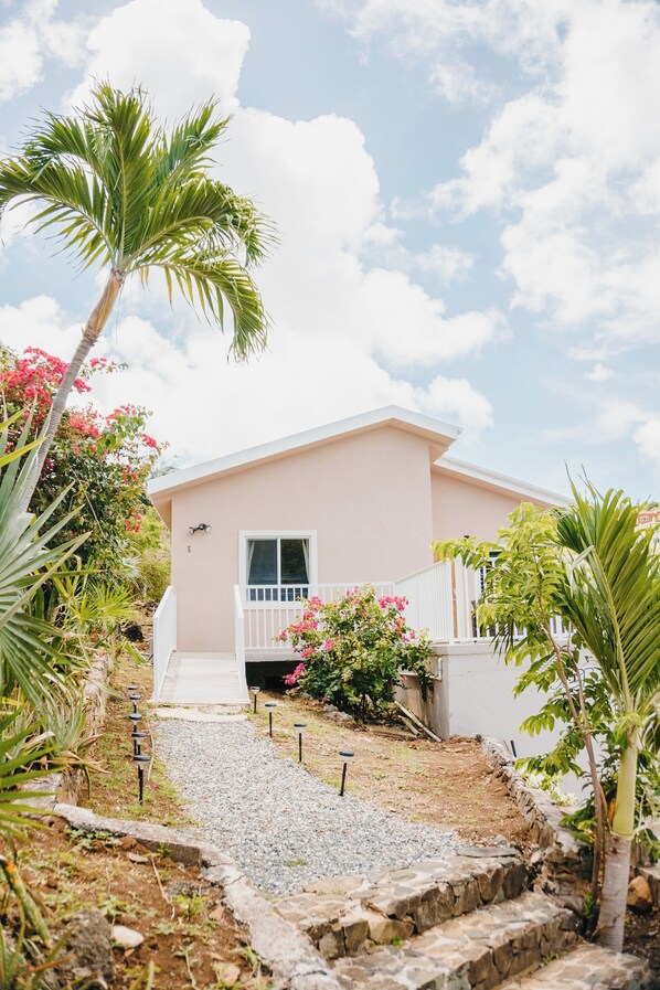 A house with a white exterior, a front porch, and a pathway leading to the entrance. - Cozy accommodations in a great location. (Cruz Bay)