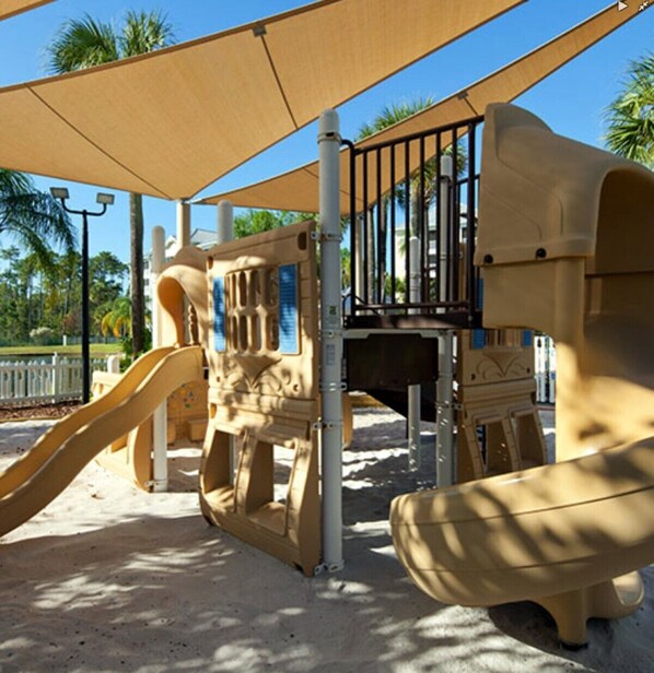 Un parque infantil con un tobogán, estructuras para escalar y una zona con sombra.