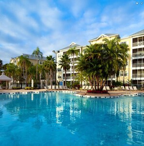 Un hotel con piscina rodeada de palmeras y sillas de descanso.