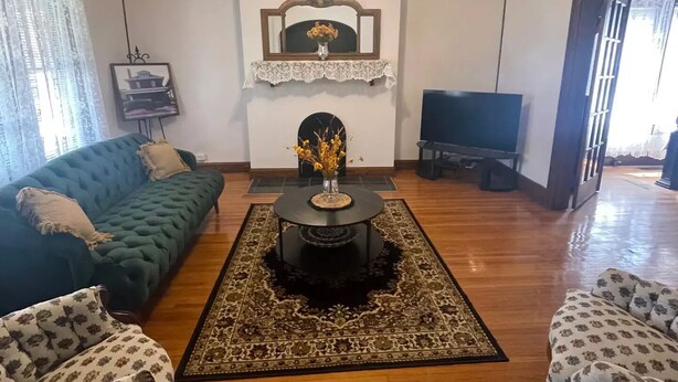 Un salon avec un canapé vert, un fauteuil à motifs, une table basse surmontée d’un vase, un téléviseur  à écran plat et un miroir décoratif.