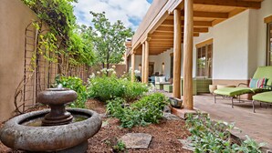 A courtyard with a stone fountain, lush greenery, and outdoor seating under a wooden pergola.