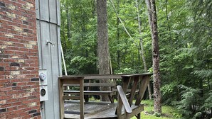 A wooden deck with steps leading to a bench, surrounded by a brick wall and a forested area.