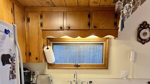 A kitchen with wooden cabinets, a window above the sink, a refrigerator, a toaster, and a patterned rug.