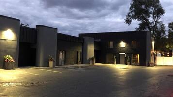 A parking lot with a building entrance, potted plants, and a tree.