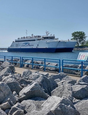 A large ferry named "Lake Express" docked at a pier with a rocky shoreline and a clear sky.