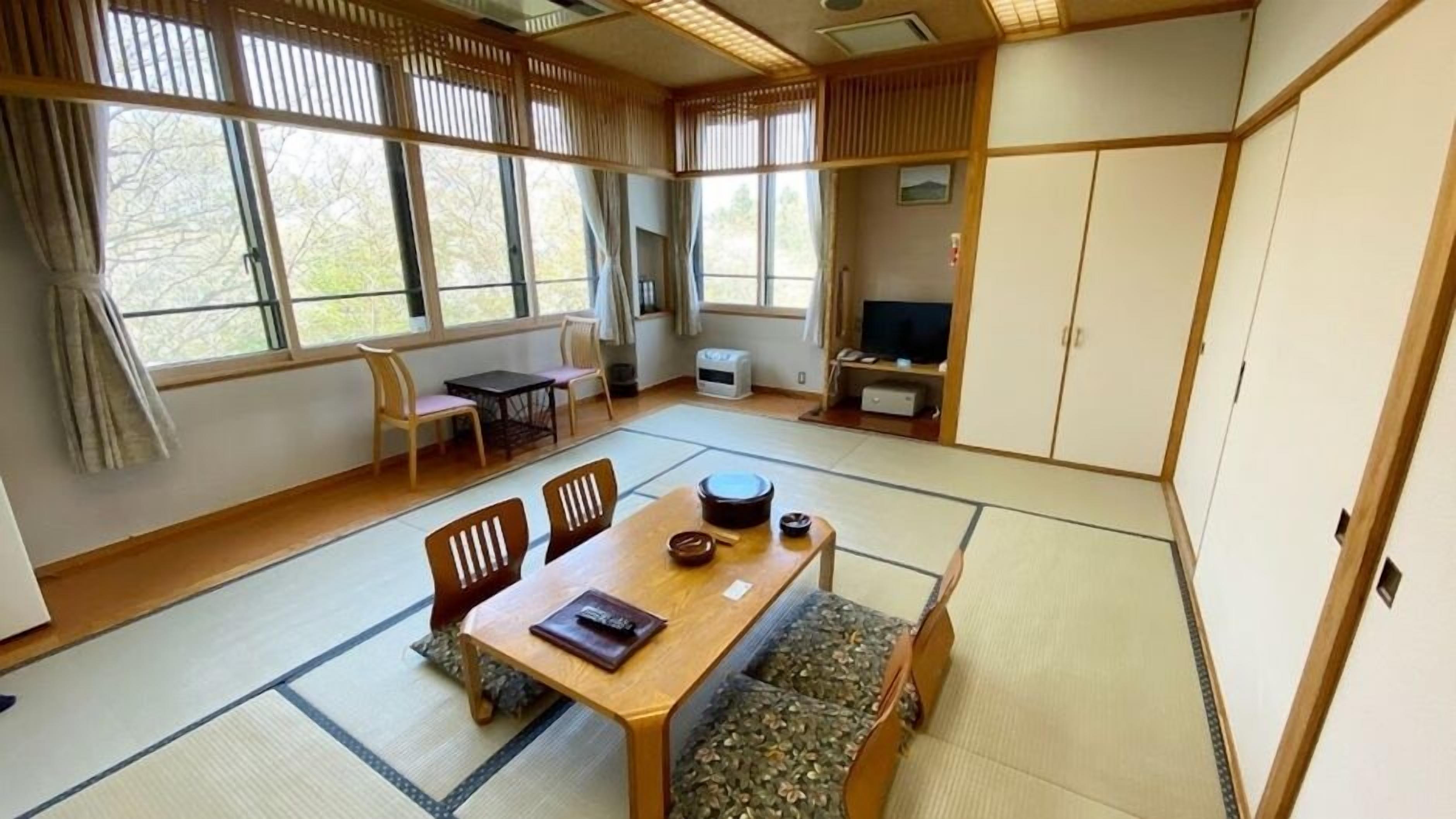 Perinteinen japanilaistyylinen huone, jossa on tatamimatto, matala pöytä tyynyineen ja liukuvat ovet.