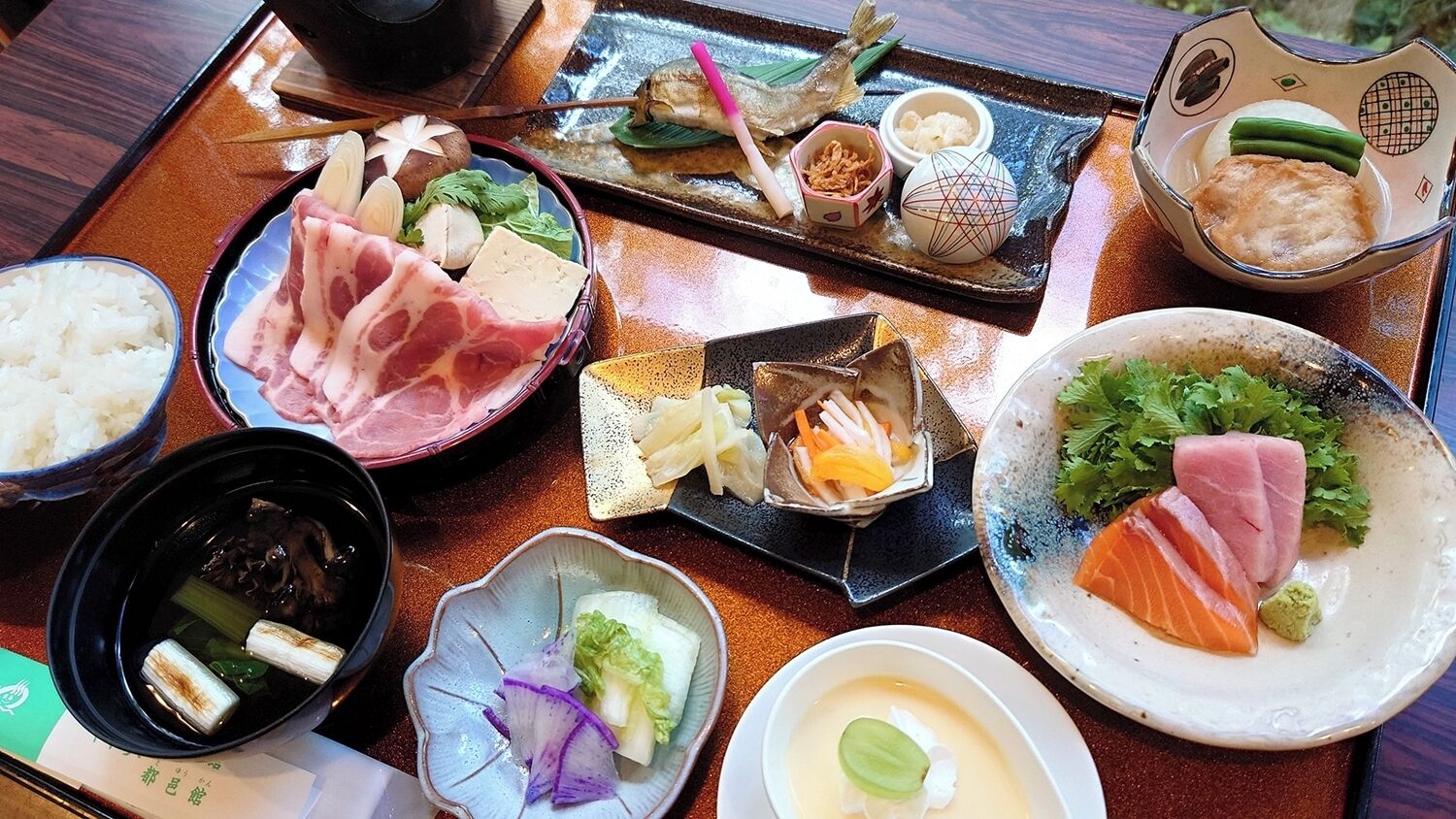 A variety of dishes on a wooden table, including sashimi, rice, and soup.