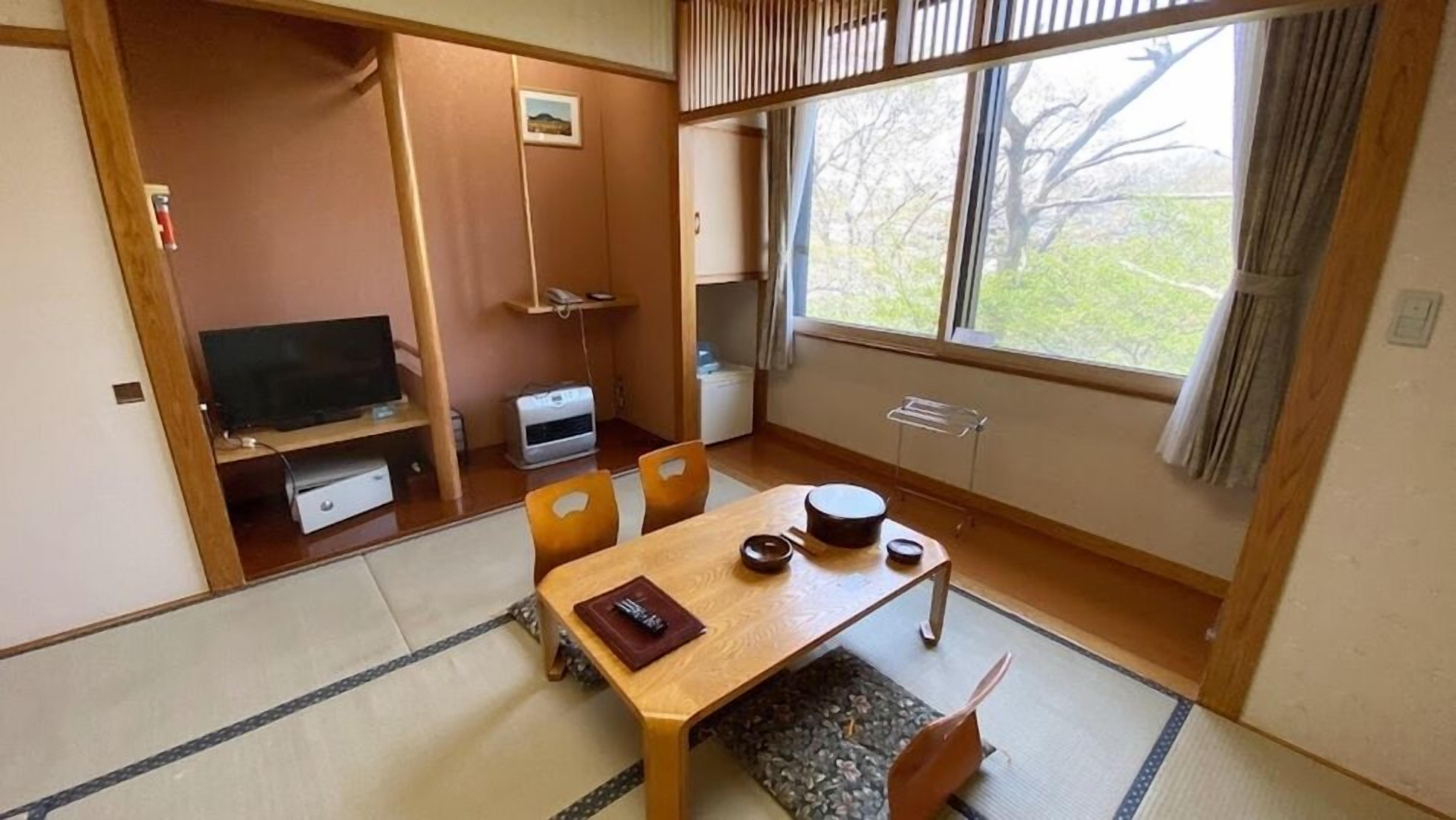 Perinteinen japanilaistyylinen huone, jossa on tatamimatto, matala pöytä teekupit ja -välineet, televisio ja ikkuna, josta avautuu näkymä puille.