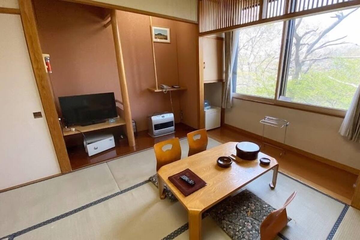 Perinteinen japanilaistyylinen huone, jossa on tatamimatto, matala pöytä teekupit ja -välineet, televisio ja ikkuna, josta avautuu näkymä puille.