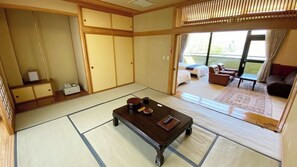 Perinteinen japanilainen huone, jossa on tatamimatto, matala puupöytä ja liukuovet, jotka johtavat parvekkeelle, jossa on ulkotilaa istumiseen.