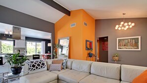 A modern living room with a sectional sofa, a glass coffee table, and a kitchen in the background. - Palm Springs Perfection - Orange Pop Palm Springs (Palm Springs)