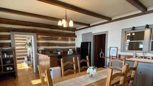 A cozy dining area with a wooden table and chairs, a chandelier, and a kitchen in the background.