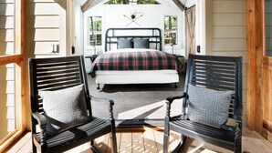 A bedroom with a bed, two chairs, a chandelier, and a view of the outdoors.