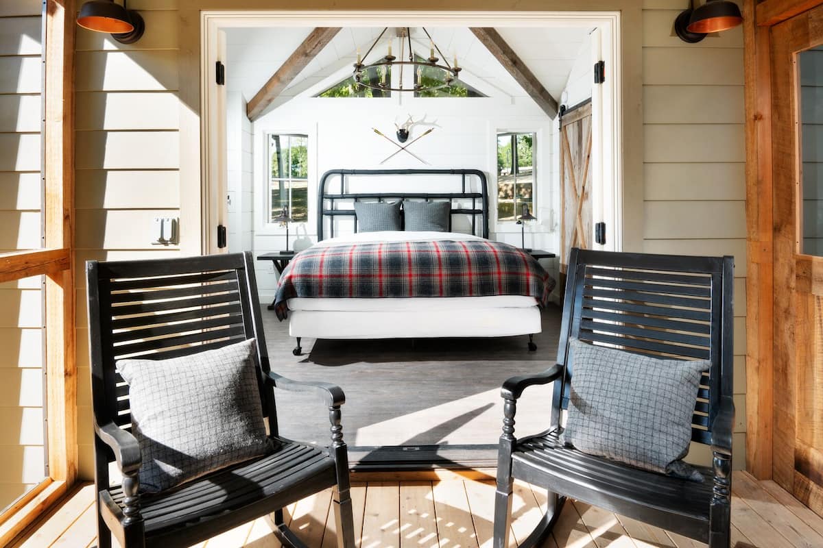 A bedroom with a bed, two chairs, a chandelier, and a view of the outdoors.