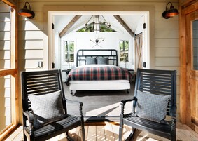 A bedroom with a bed, two chairs, a chandelier, and a view of the outdoors.