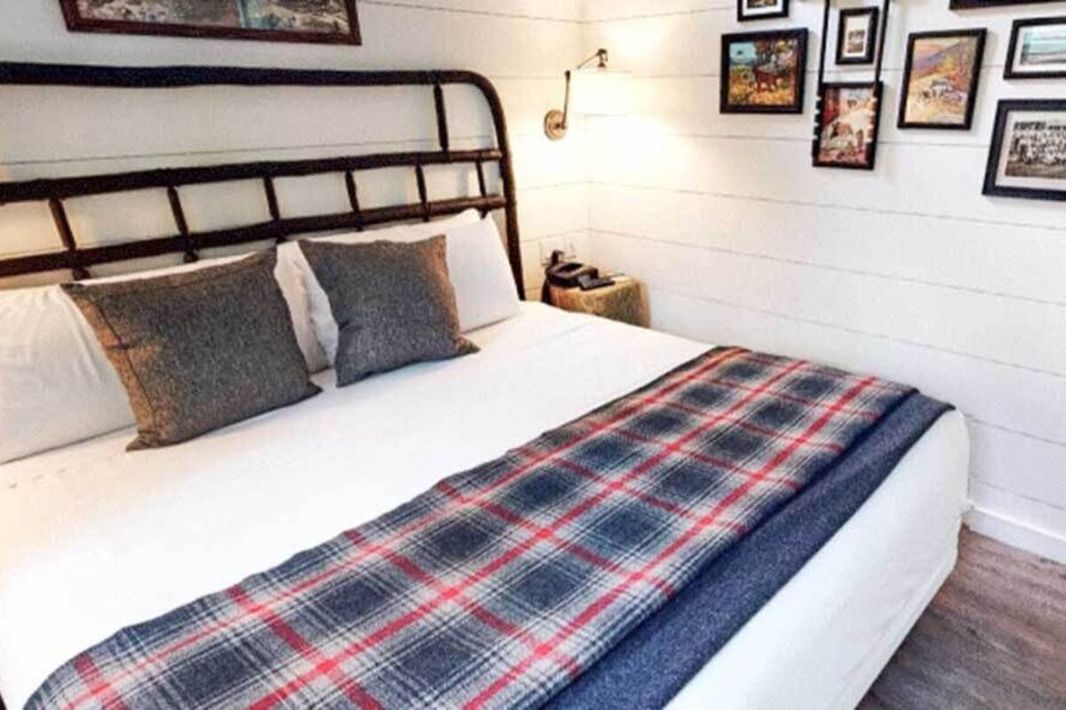 A neatly made bed with a plaid blanket, a wooden headboard, and a bedside table with a lamp.