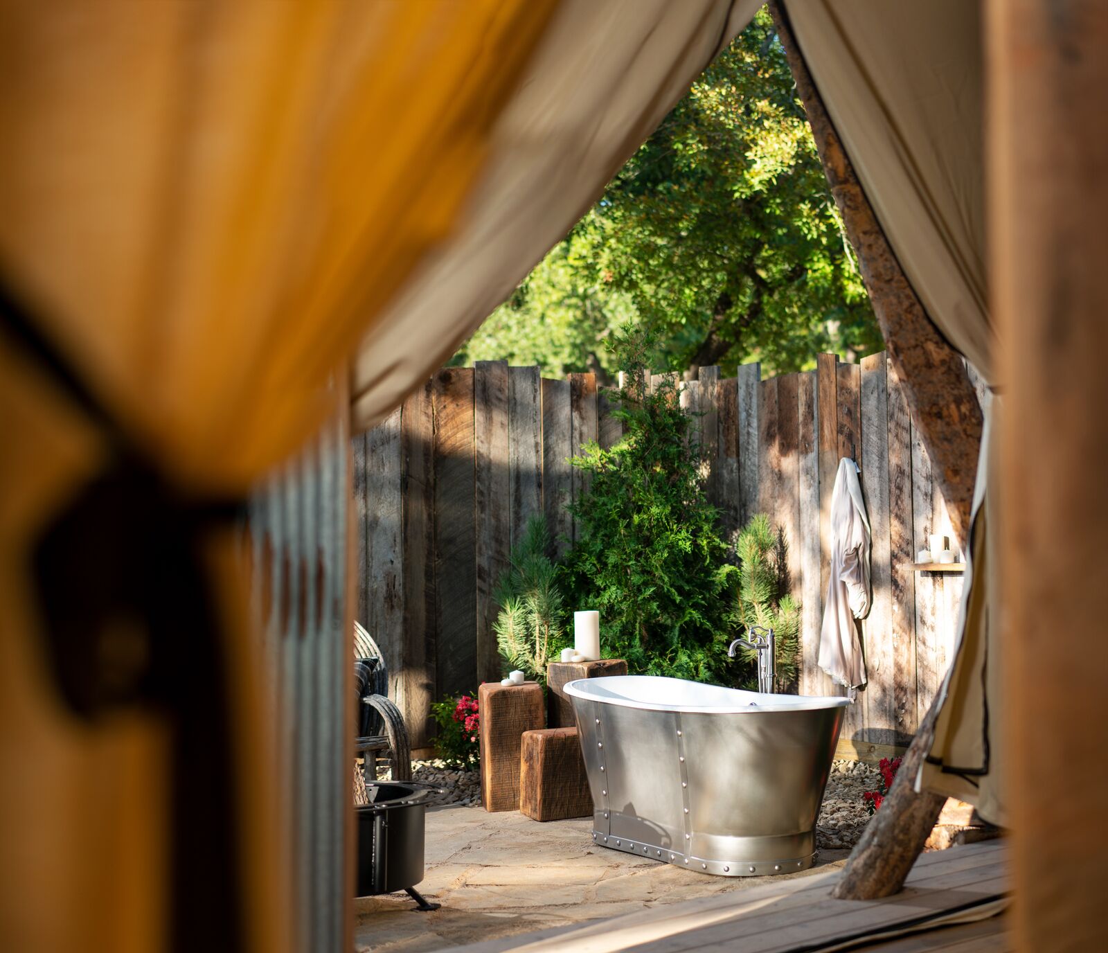 An outdoor spa area with a large freestanding bathtub, wooden fence, and greenery.