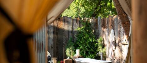 An outdoor spa area with a large freestanding bathtub, wooden fence, and greenery.
