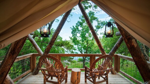 A rustic wooden deck with two wicker chairs and a small table, overlooking a forested area.