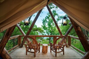 A rustic wooden deck with two wicker chairs and a small table, overlooking a forested area.