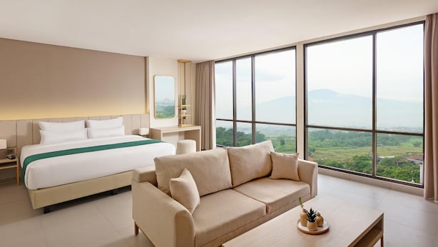 Habitación de hotel con una cama grande, un sofá, una mesa de centro y vistas al campo.