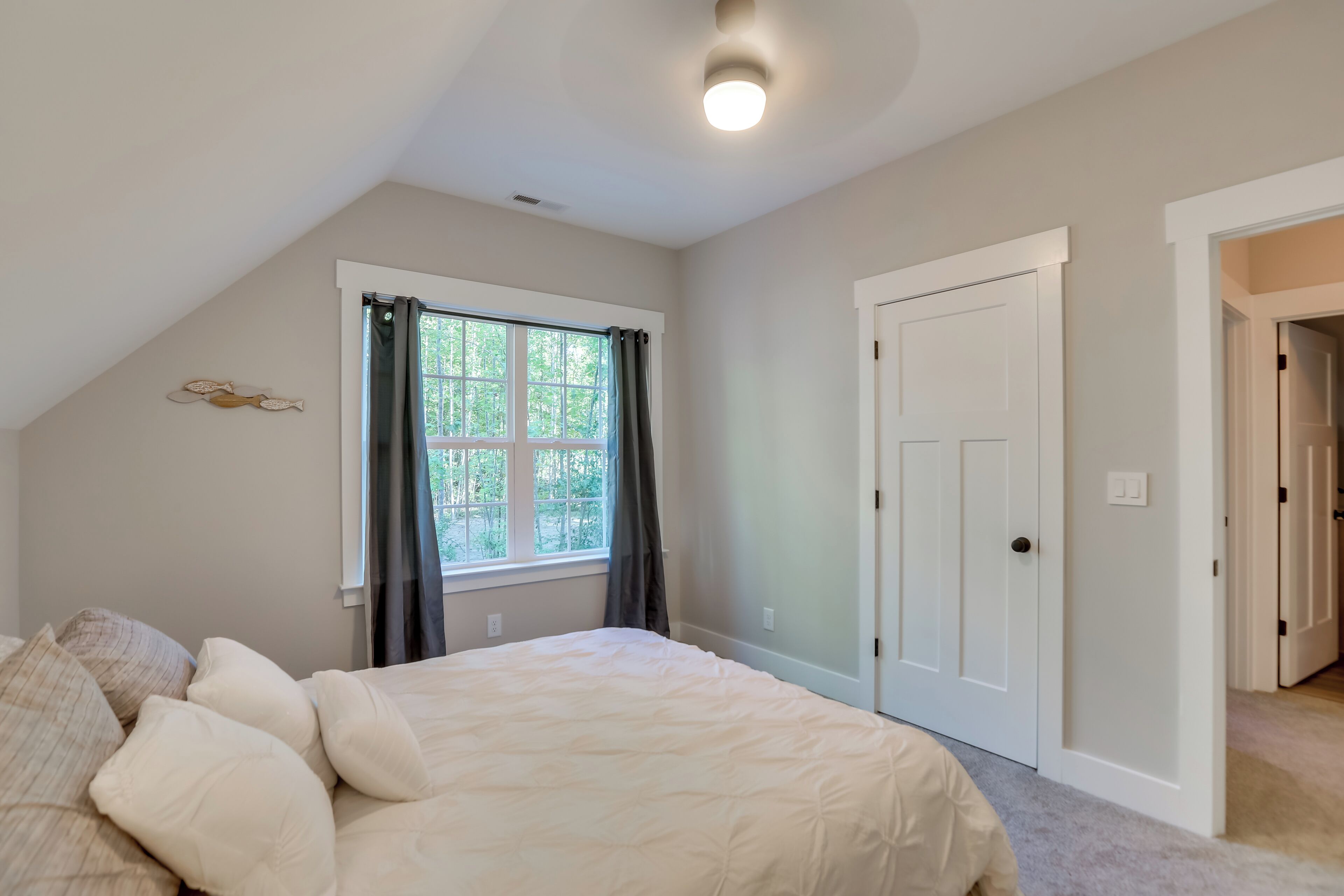 A bedroom with a large bed, a window with curtains, a door, and a ceiling light.