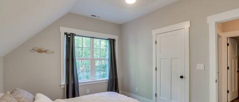 A bedroom with a large bed, a window with curtains, a door, and a ceiling light.