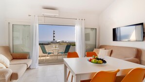 Ein modernes Hotelzimmer mit Balkon, einem Esstisch mit Obst und einem Fernseher an der Wand.