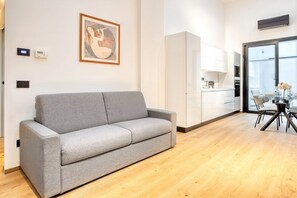 A modern living room with a grey sofa, a dining area with a glass table, and a kitchen in the background.