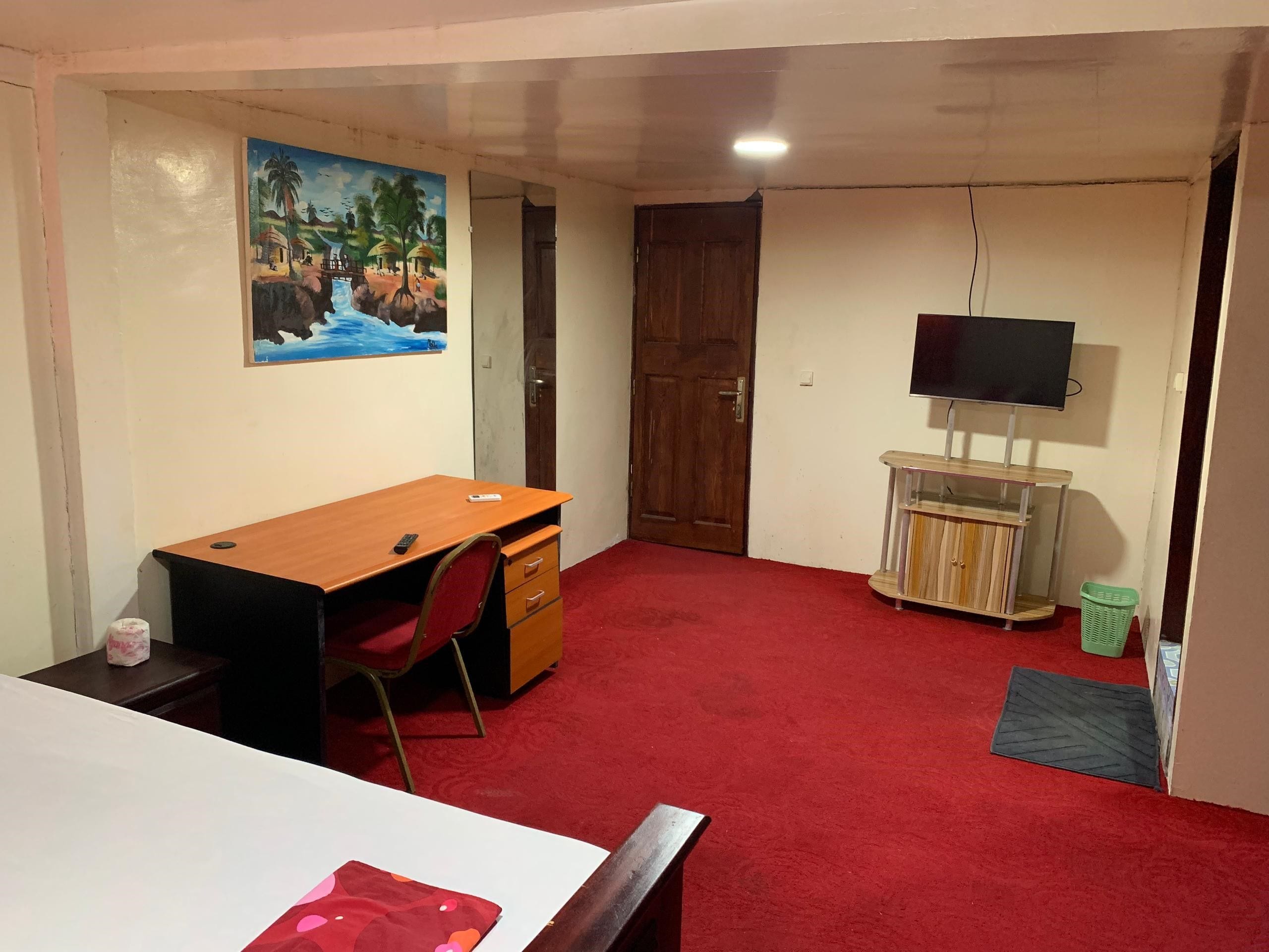 Una habitación con un escritorio de madera, alfombra roja, televisor y un cuadro en la pared.