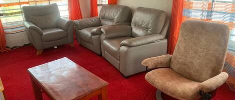 A living room with a red carpet, two leather sofas, a wooden coffee table, and a single armchair.